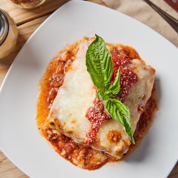 A delicious lasagna with melted cheese, rich red sauce, and fresh basil on a white plate.