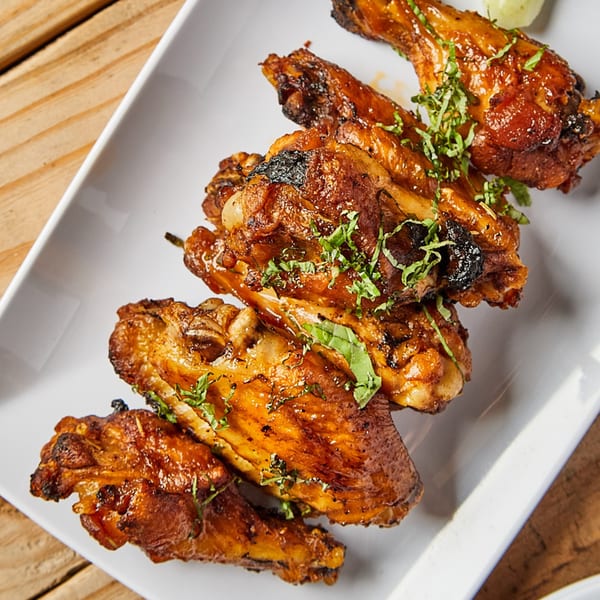 Close-up of Piabella's wood-fired chicken wings, glazed and garnished with fresh herbs on a white plate.