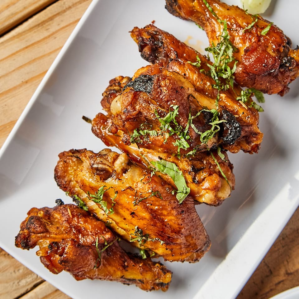 Close-up of Piabella's wood-fired chicken wings, glazed and garnished with fresh herbs on a white plate.