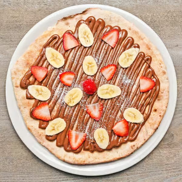 Piabella Wood-Fired Pizza's dessert pizza with Nutella, sliced bananas, and strawberries on a white plate.