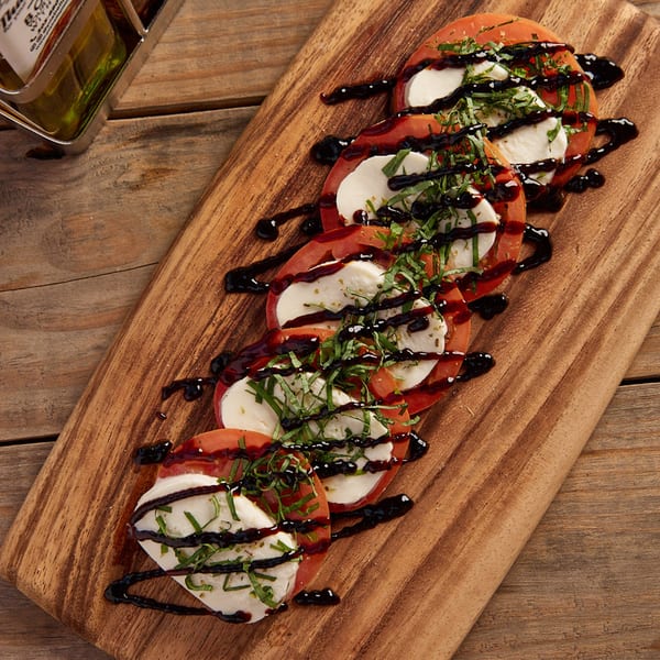 Caprese salad with sliced tomatoes, mozzarella, basil, and balsamic glaze on a wooden board.