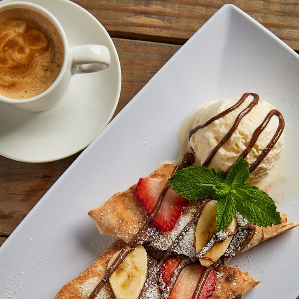 Dessert pizza with strawberries, bananas, chocolate, powdered sugar, mint, vanilla ice cream, and coffee.